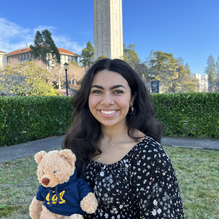 Color photo of Seemani holding a bear plushie in front of the Campanile