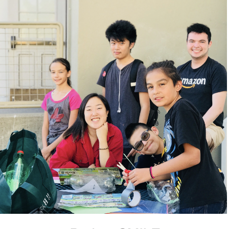 Photo of Project Smile club members smiling while sitting at an outdoor crafting table