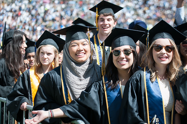 Multiple Berkeley students outside in graduation regalia, shouting in joy and celebrating.