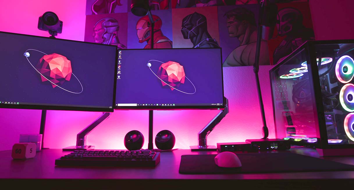 A dual monitor adjustable height gaming desk setup lit up red and purple with LEDs