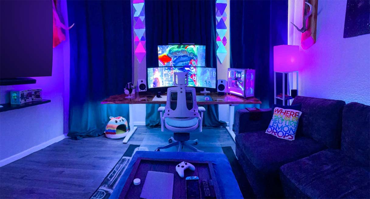 An ergonomic UPLIFT standing desk with a Pursuit Chair and dual monitor arm in a gaming room with LED lights