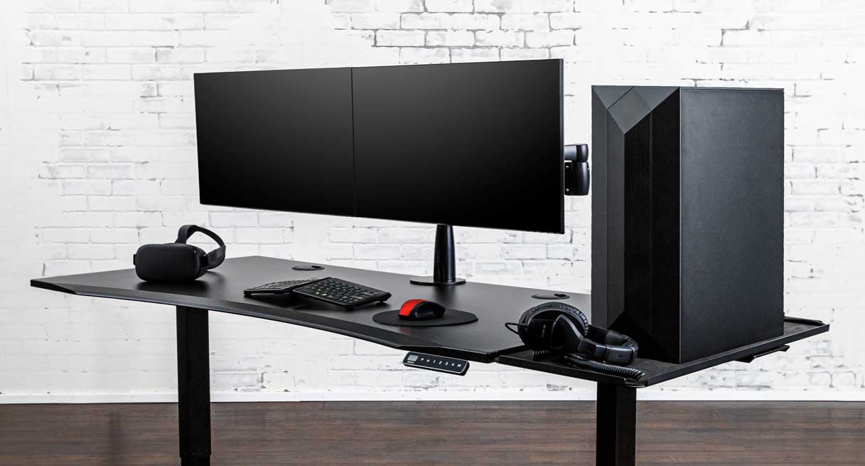 A gaming setup with dual monitors, ergonomic keyboard, gaming tower on UPLIFT Desk Extension, and other accessories on an UPLIFT eco curve sit stand desk