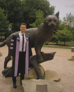 Photo shows Dr. Wilt in graduation attire in front of the UK Wildcat statue