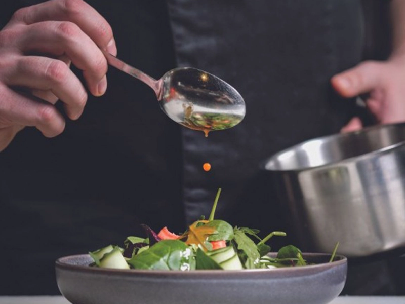 close-up of hands pouring dressing on a salad