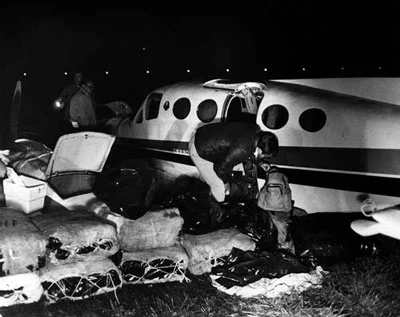 Man crouching in front of a small plane with with sacks in front of it