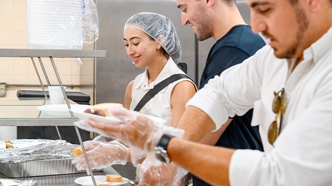 three people in the kitchen serving dishes