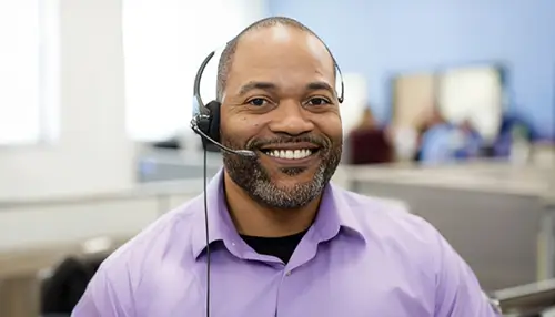 A professional male with a headset, he smiles at the camera