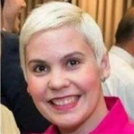 Headshot of a woman, she smiles at the camera, she has short blonde hair