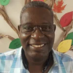 Headshot of a man, he smiles at the camera, he has on glasses