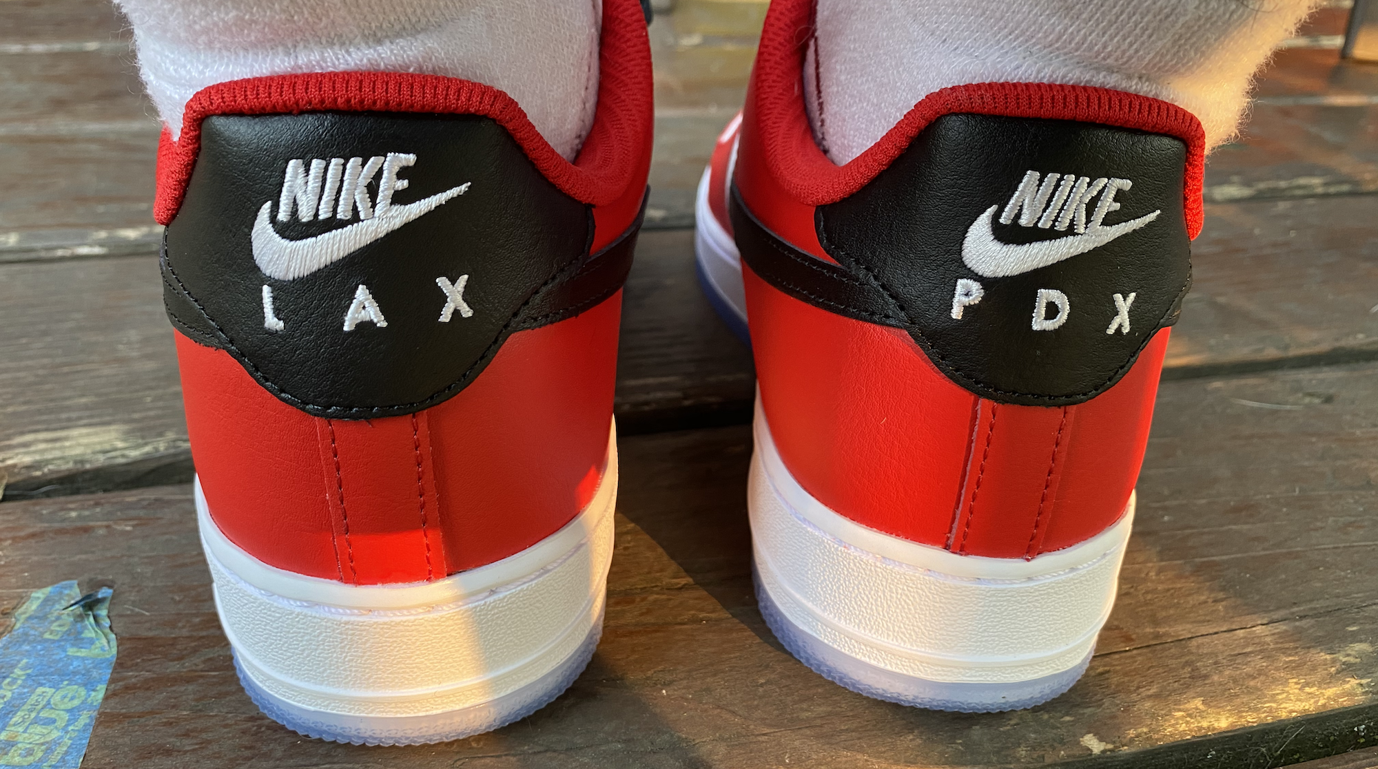 Photo of custom red sneakers with white sole, and black heel tab with white writing. "LAX" and "PDX" are printed one per heel.
