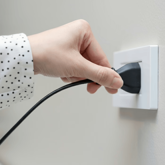 hand plugging white air conditioner power cord into wall outlet, clean modern interior, simple setup