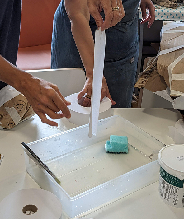 A close of a person holding a wet, white strip of gum tape over a tray of water