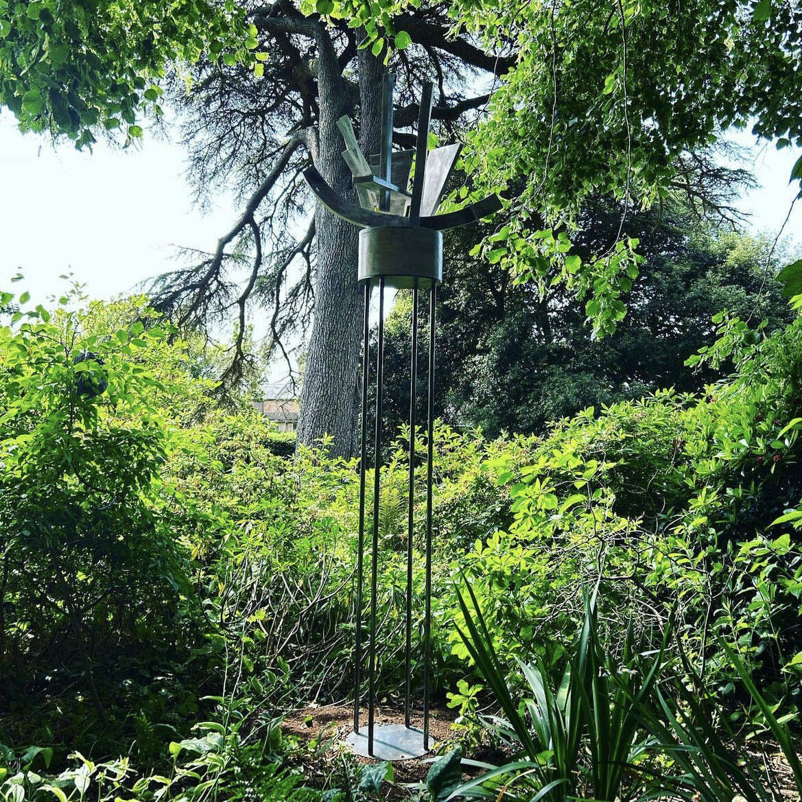 A metal sculpture in a garden, encircled by trees.