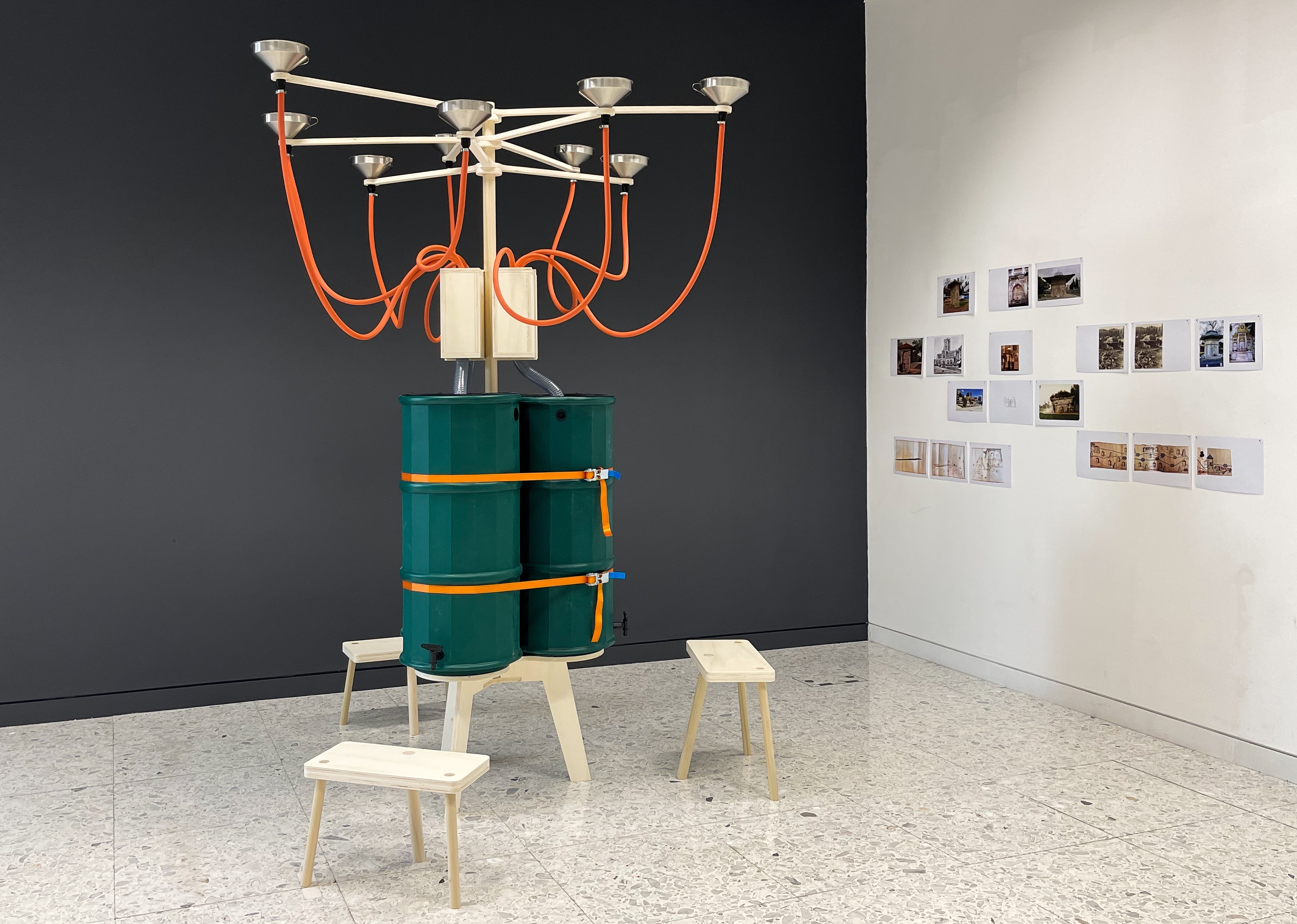 A sculpture crafted from pipes and water butts, presented in a gallery space.