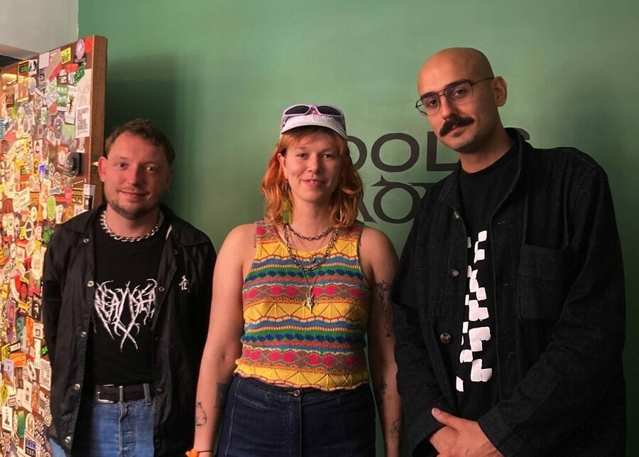 Three people standing in front of a green wall.