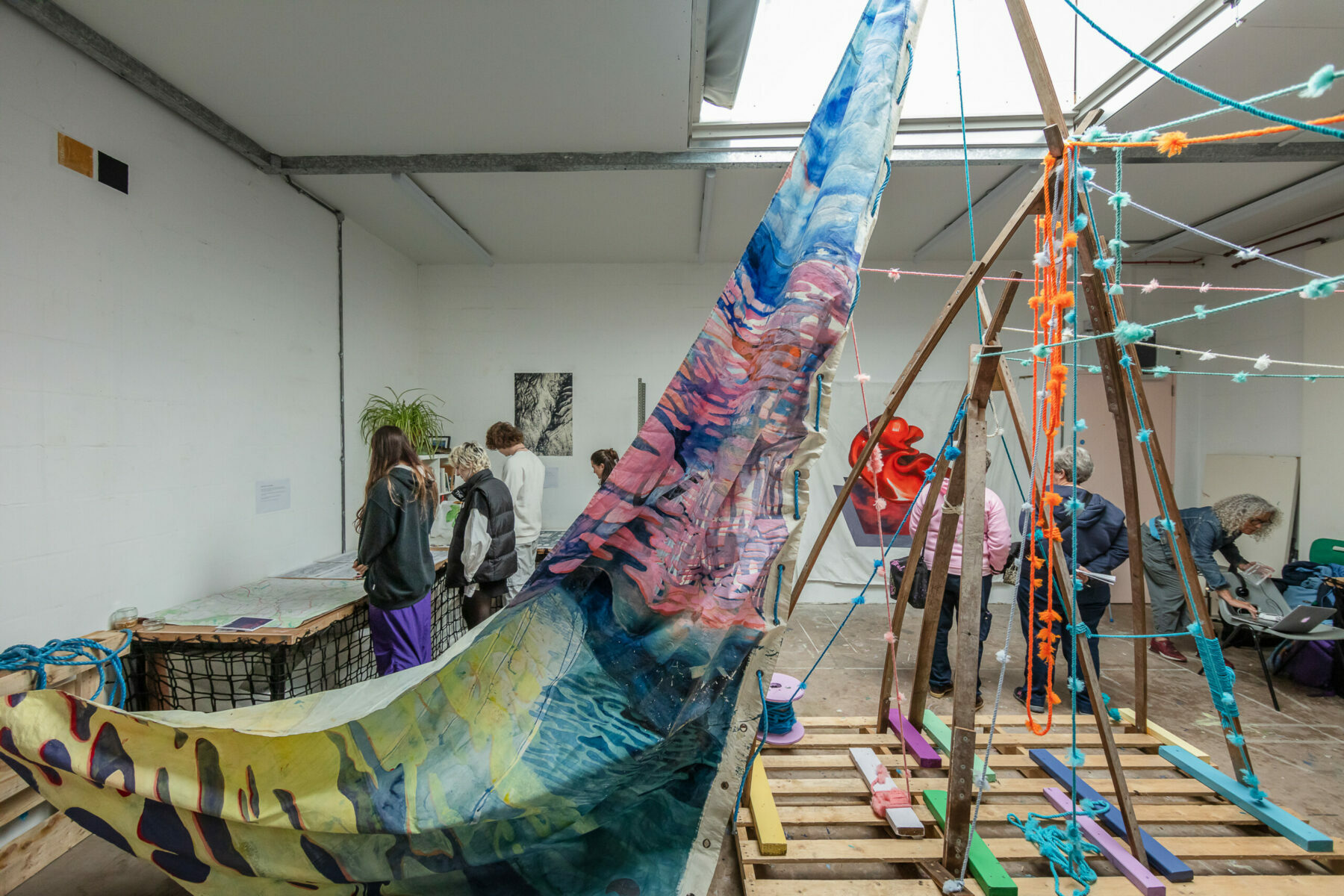 People looking at an installation of an artwork including a large wooden frame sculpture with a painted sail.