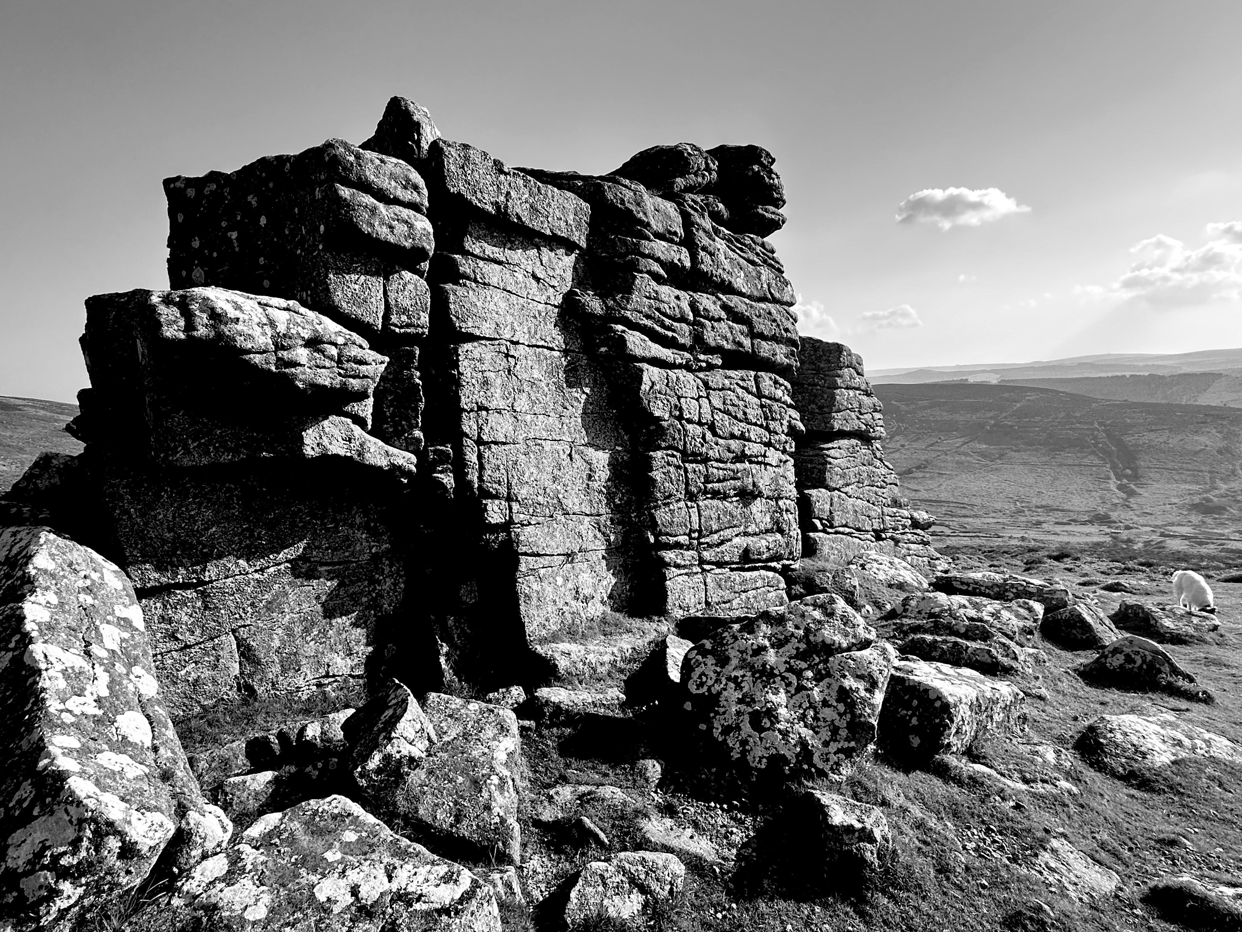 A stone Tor on Dartmoor is in the foreground of the image with hills in the distance