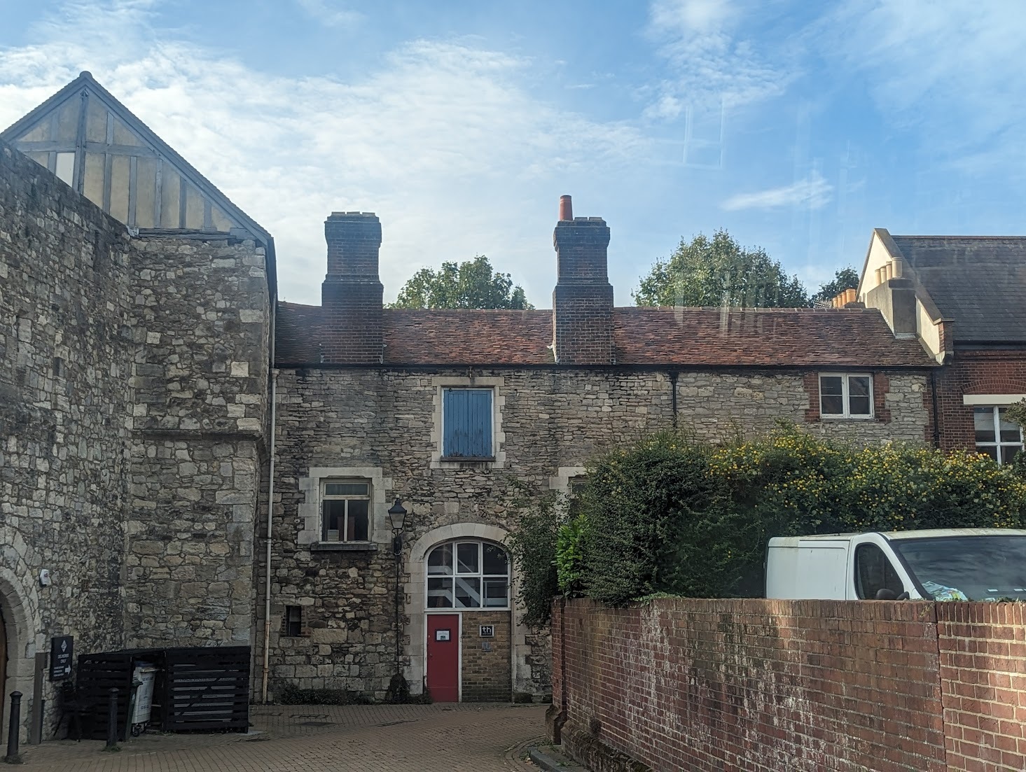 An image of the front of a series of stone buildings, there is an entrance with a red door and glass window arch