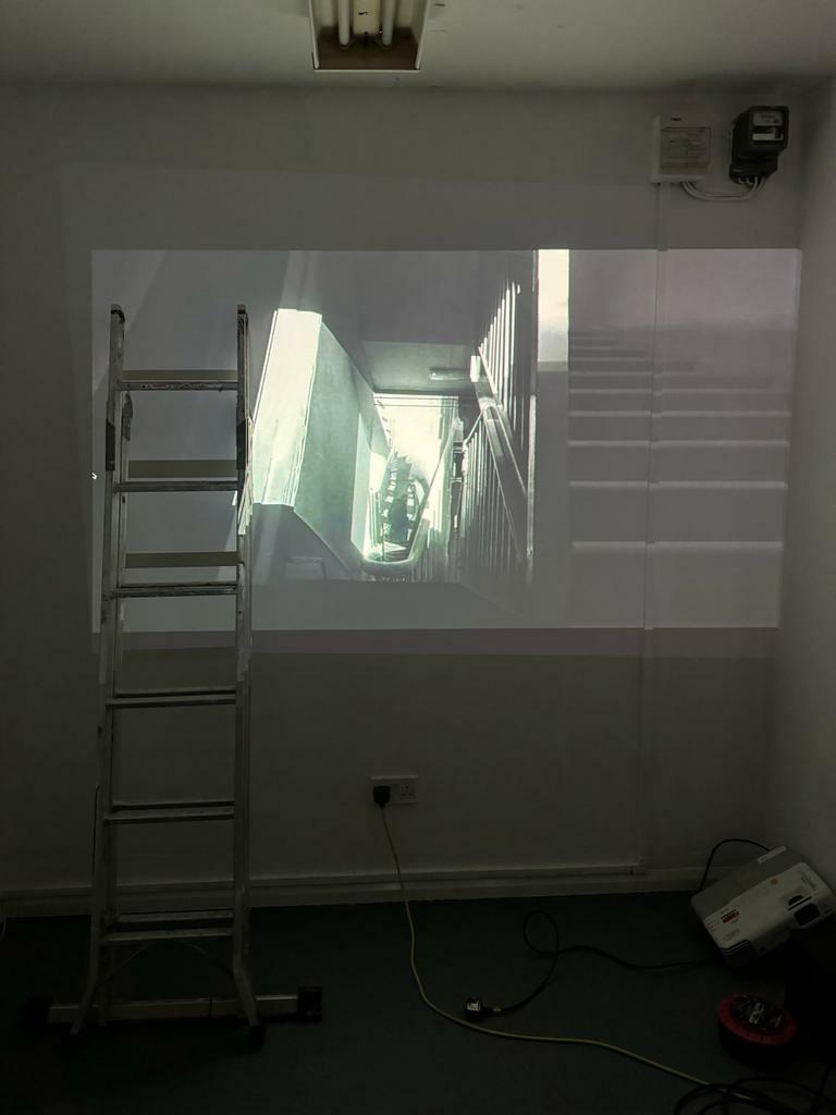A projected image of a corridor and stairway on a wall, with a ladder leaning onto the wall and on top of the projected image