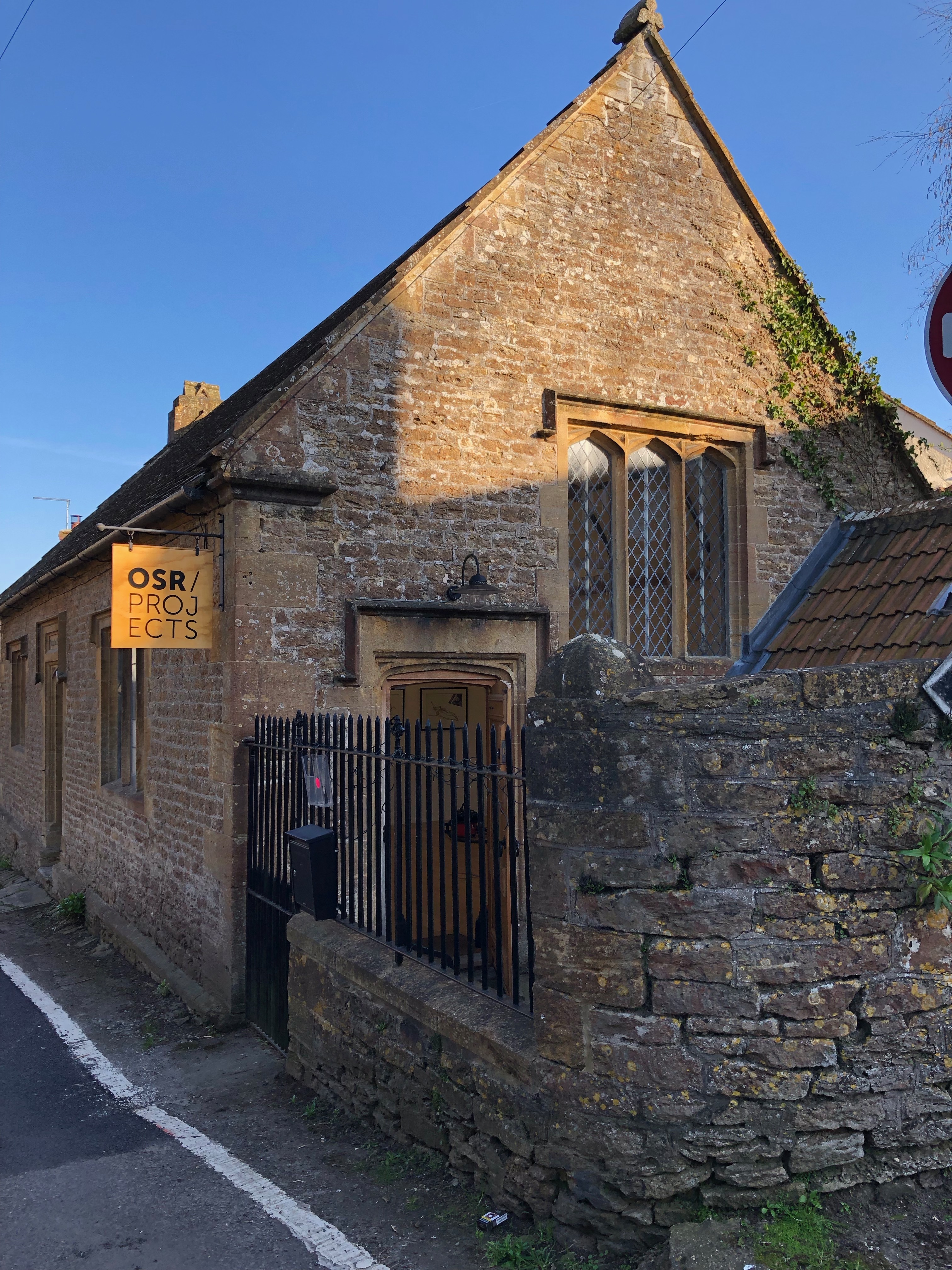 A stone building with a wooden sign jutting out from the building on a pole that says 'OSR PROJECTS'