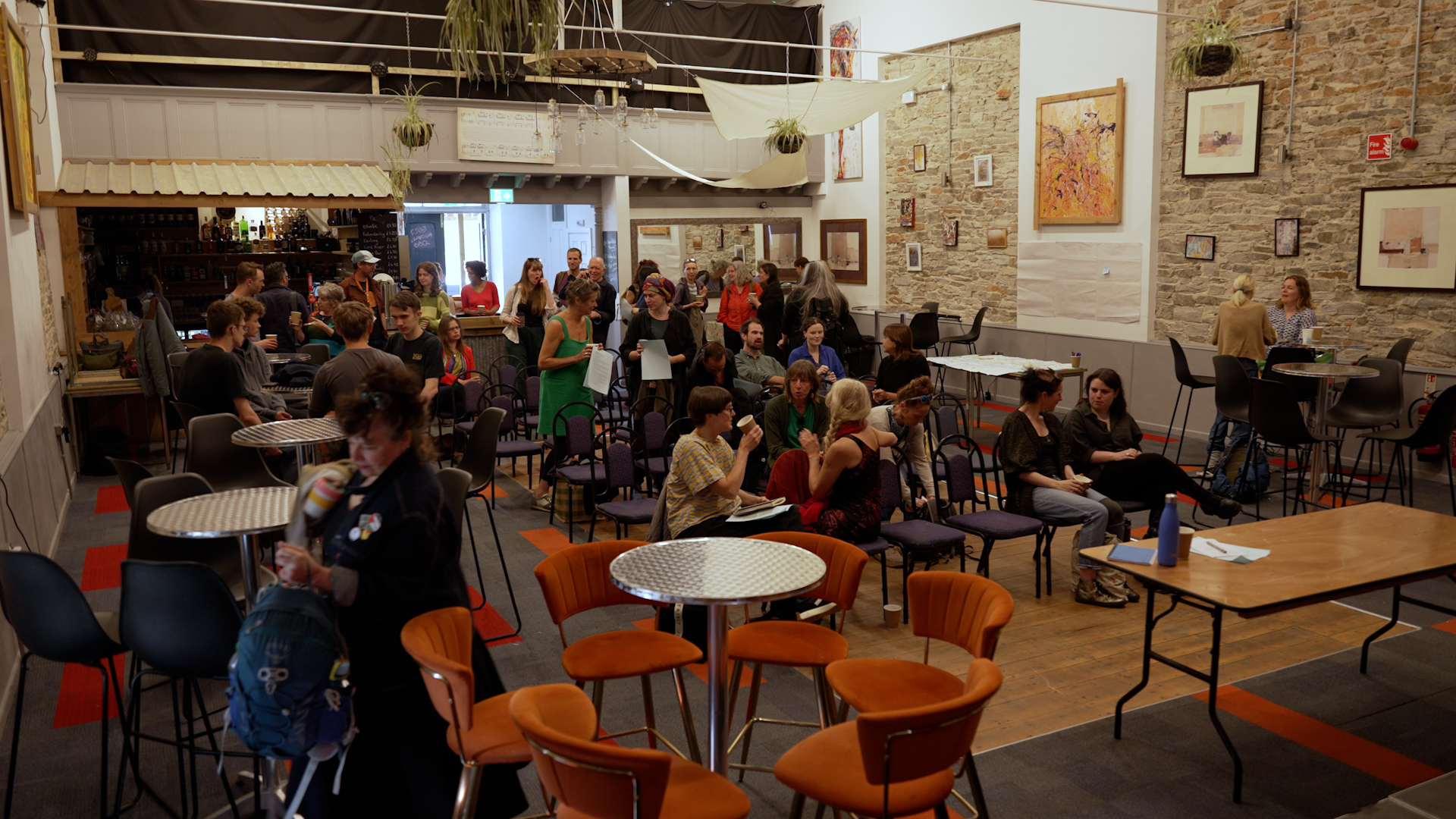 A room full of people are sat and stood around chatting and drinking coffee in groups.