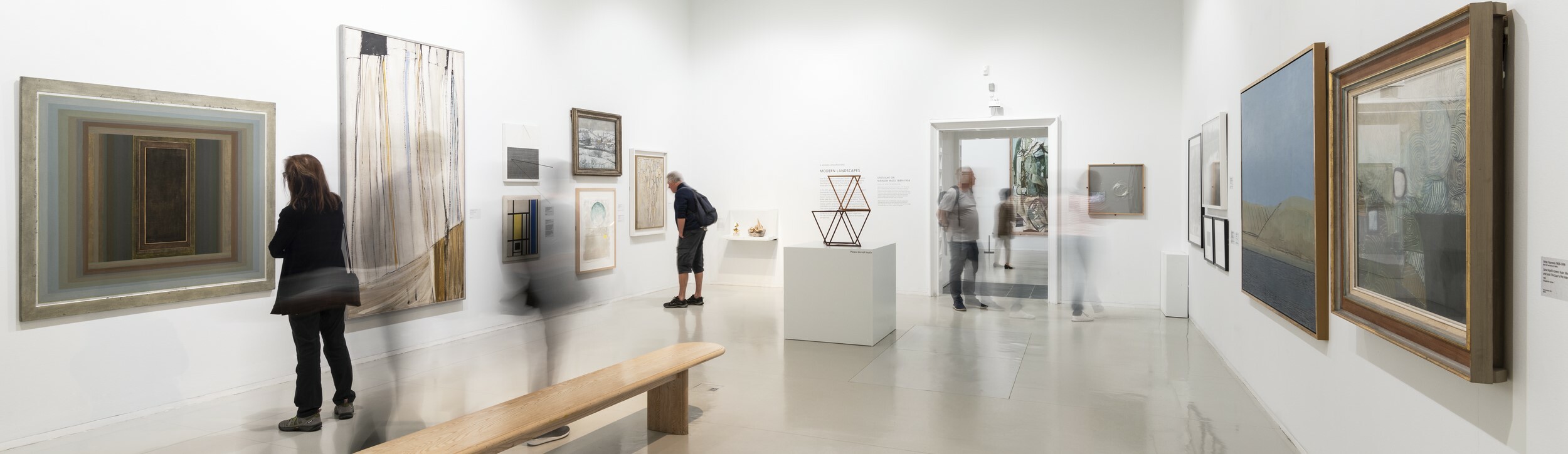 People walking through an art gallery, admiring paintings on the wall.