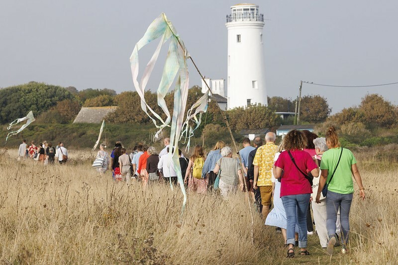 People walking through a field with their backs to the camera with a lighthouse in background