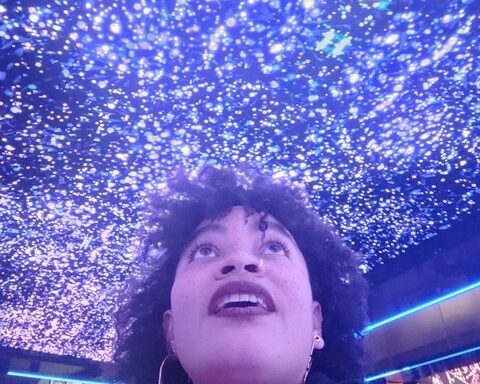 A portrait of a woman looking up to a ceiling covered in small bright lights