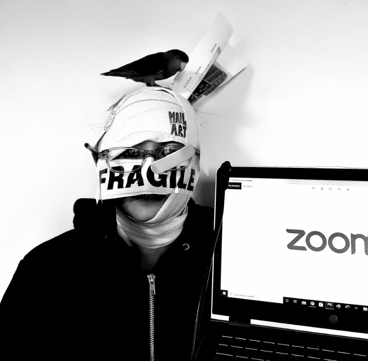 A black and white portrait photograph of Amanda Lynch, holding a laptop with Zoom text, bandages around head with Bobby the love bird