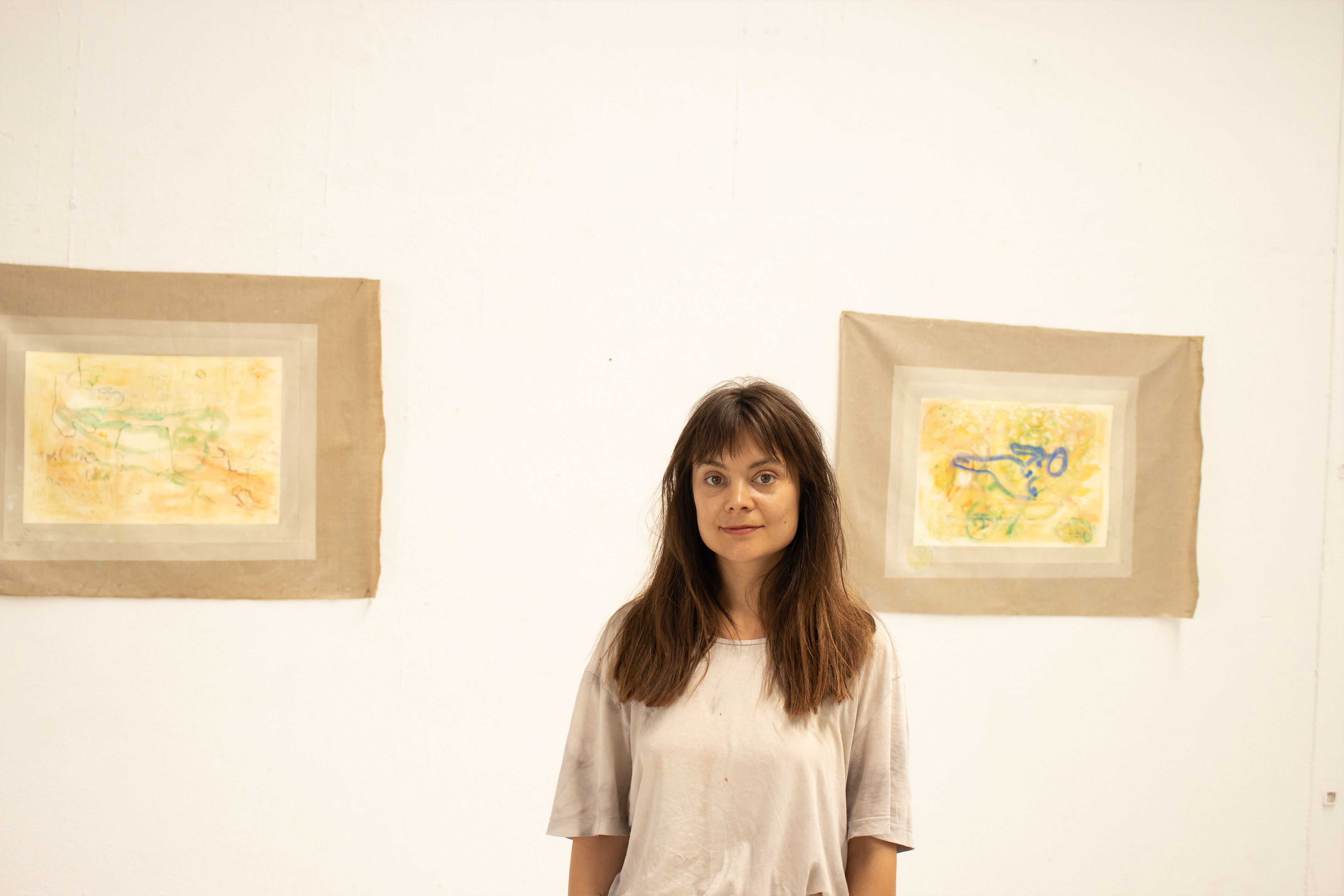 A white woman with long brown hair standing in front of two wall mounted artworks