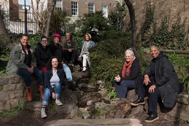 A photograph of a group of eight smiling people gathered together for a portrait in an urban garden space.