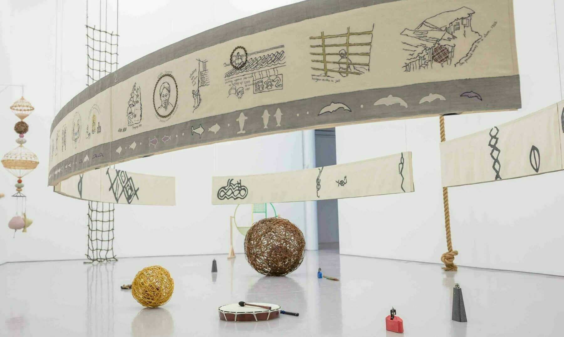 A group of sculptures in a gallery space, including an embroidered fabric panel, instruments and circular woven objects.