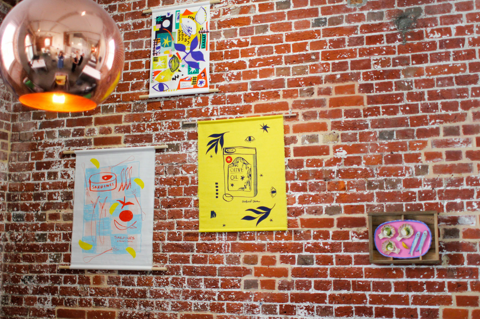 A series of colourful prints depicting food installed on a brick wall in the gallery.