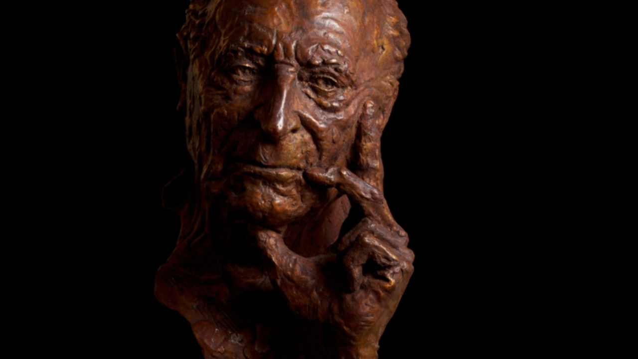 a bronze bust of a man holding a hand to his face thoughtfully
