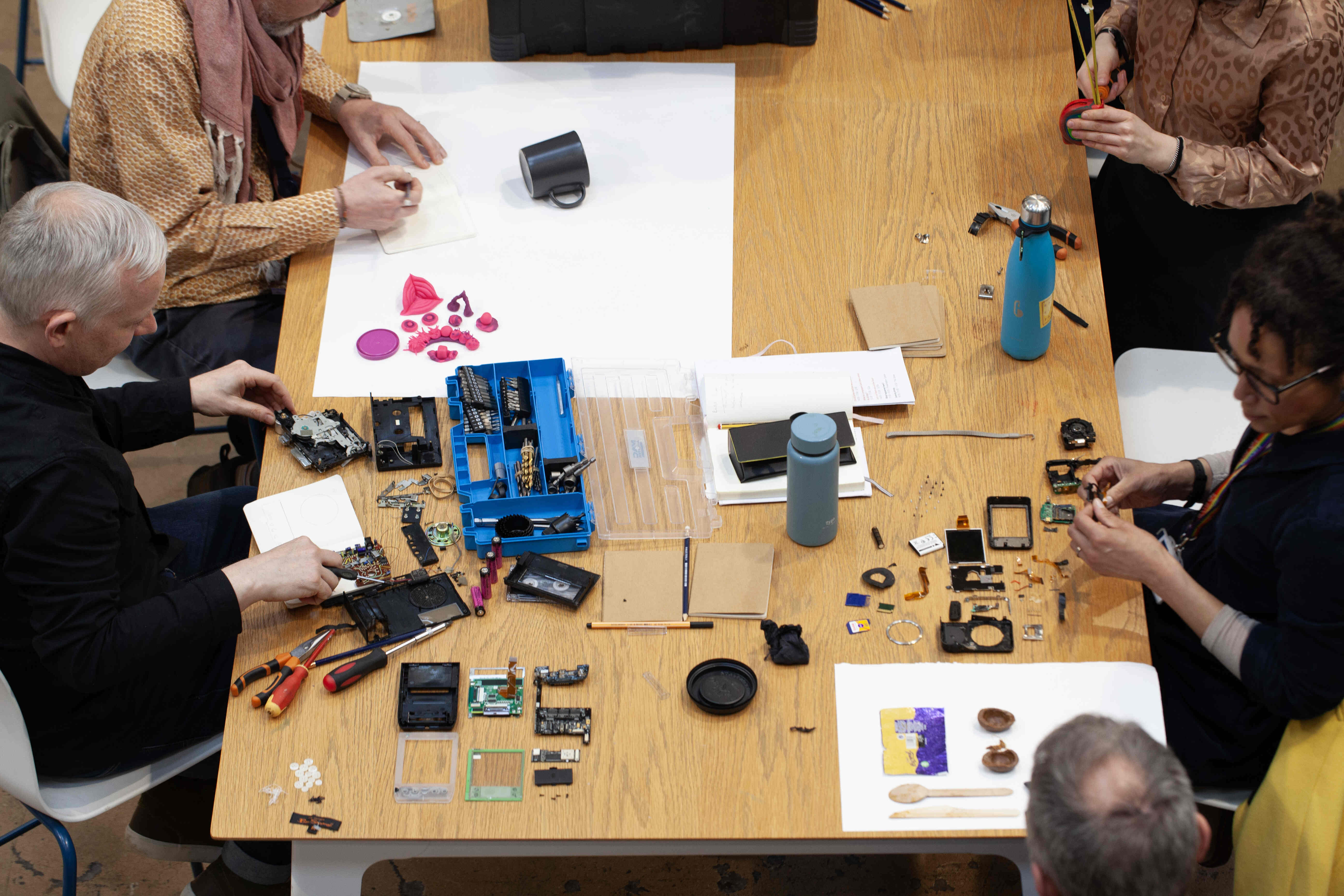 A group of people sitting at a table, taking apart a variety of items.