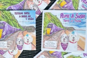 two colourful children's books titled 'Rupee and Sushi travel by train' there are two dogs on the front cover as well as a train track