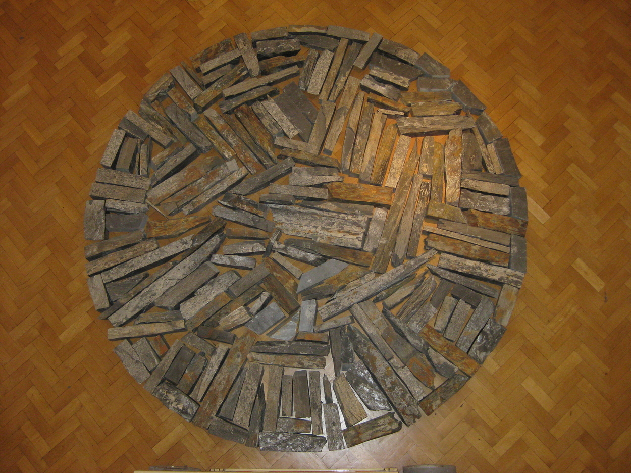 Circle composed of grey slate pieces on a honey coloured parquet floor.