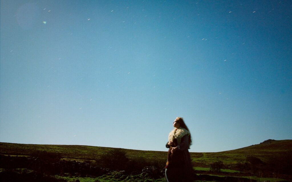 a woman wanders on a hilltop landscape and looks at a blue sky