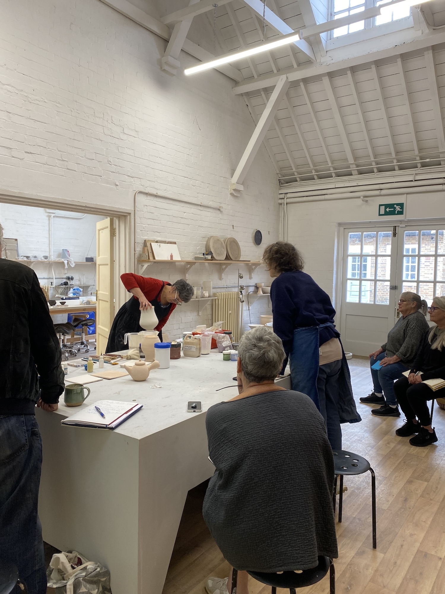Artist Tutor demonstrating glazing techniques to students in a ceramics studio