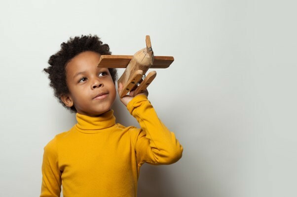 A boy plays with a wooden model plane