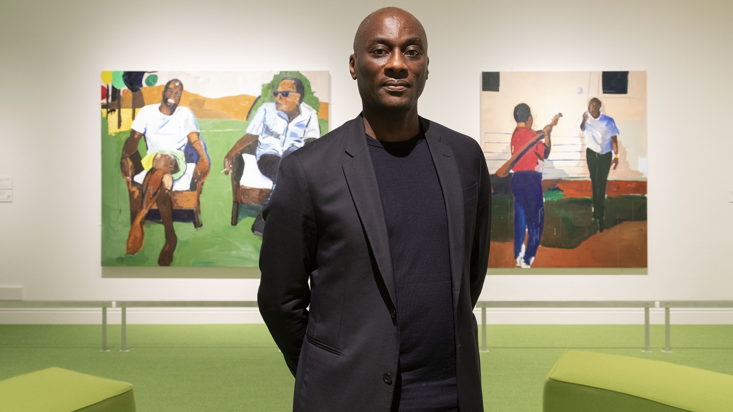 Write and curator Ekow Shun standing in front of paintings in a gallery