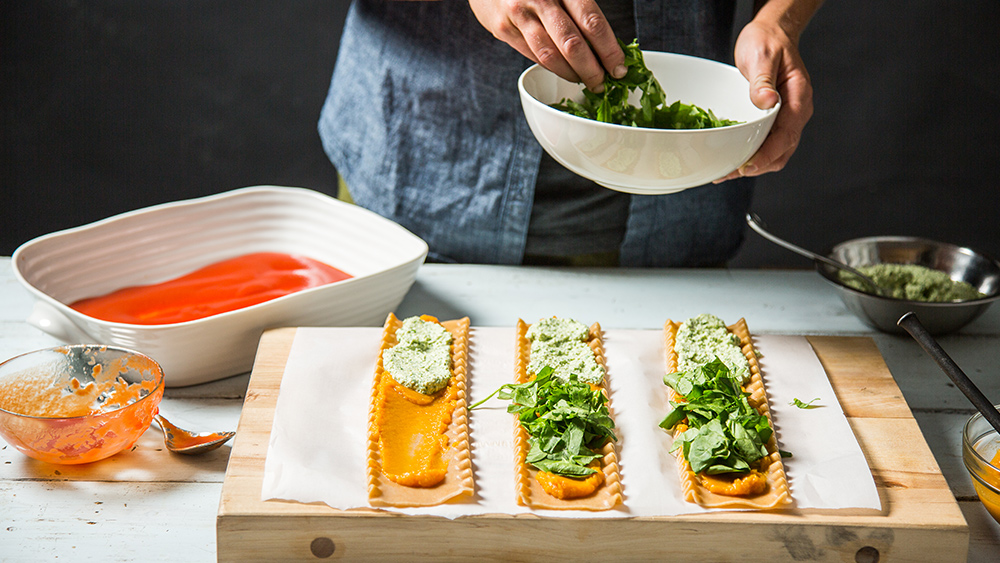 someone putting spinach on vegan lasagna rolls