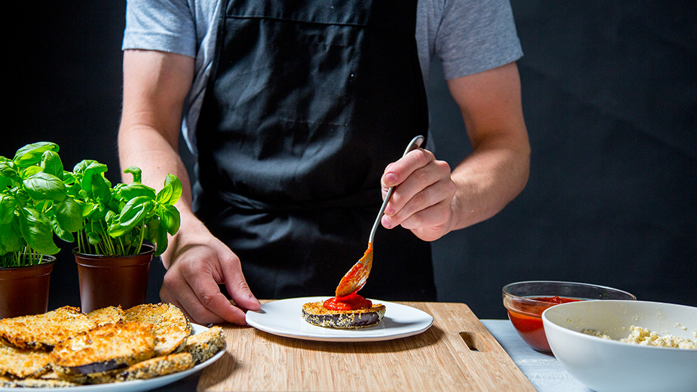 man putting sauce on vegan eggplant parmesan