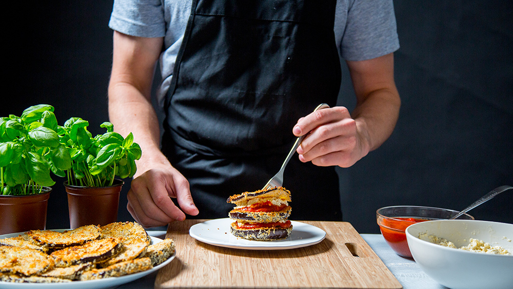 man putting sauce on vegan eggplant Parmesan