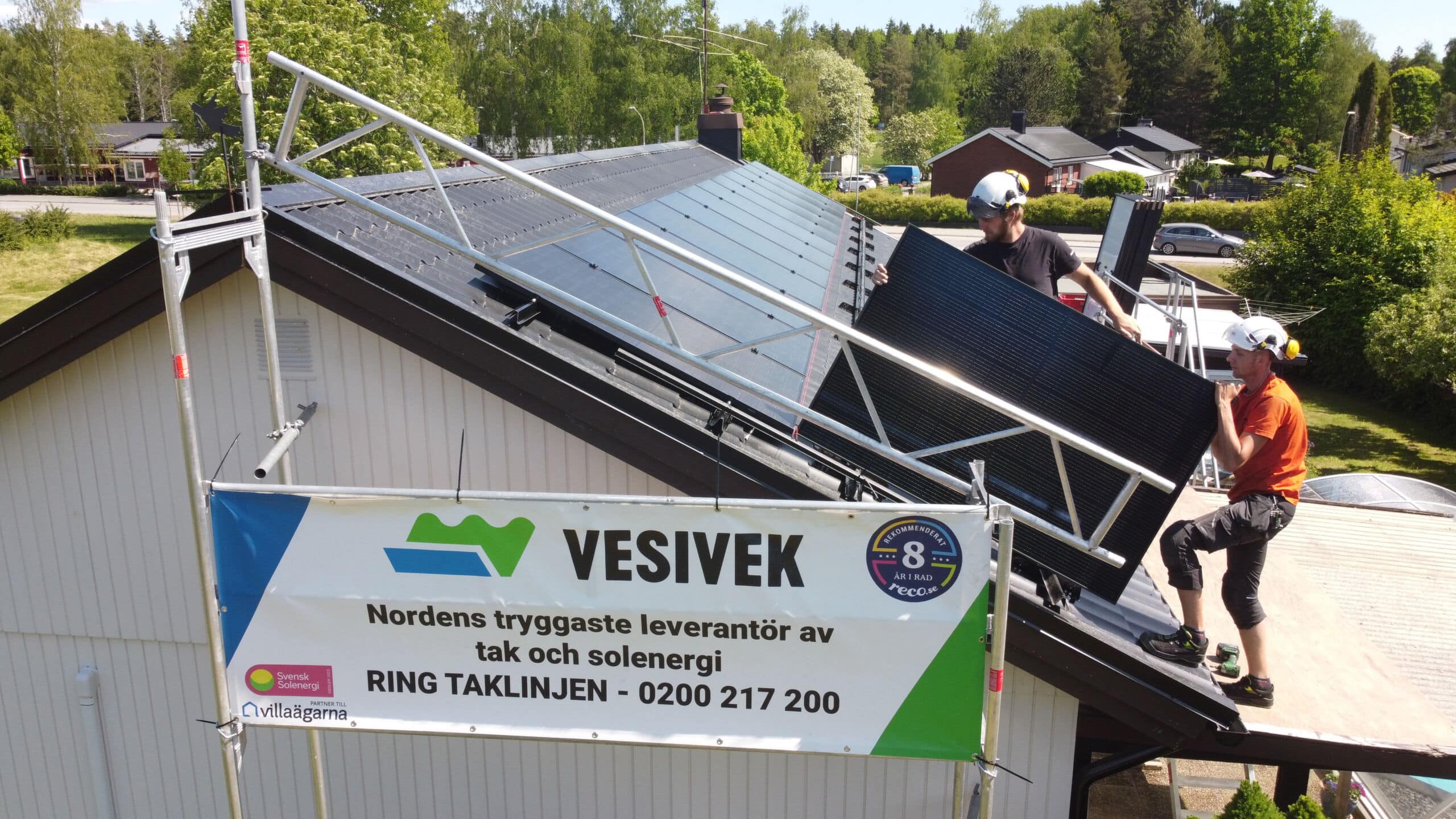 Svarta solceller på tak, banderoll i förgrunden på ställning med Vesiveks logga. 2 st solcellsinstallatörer på bild