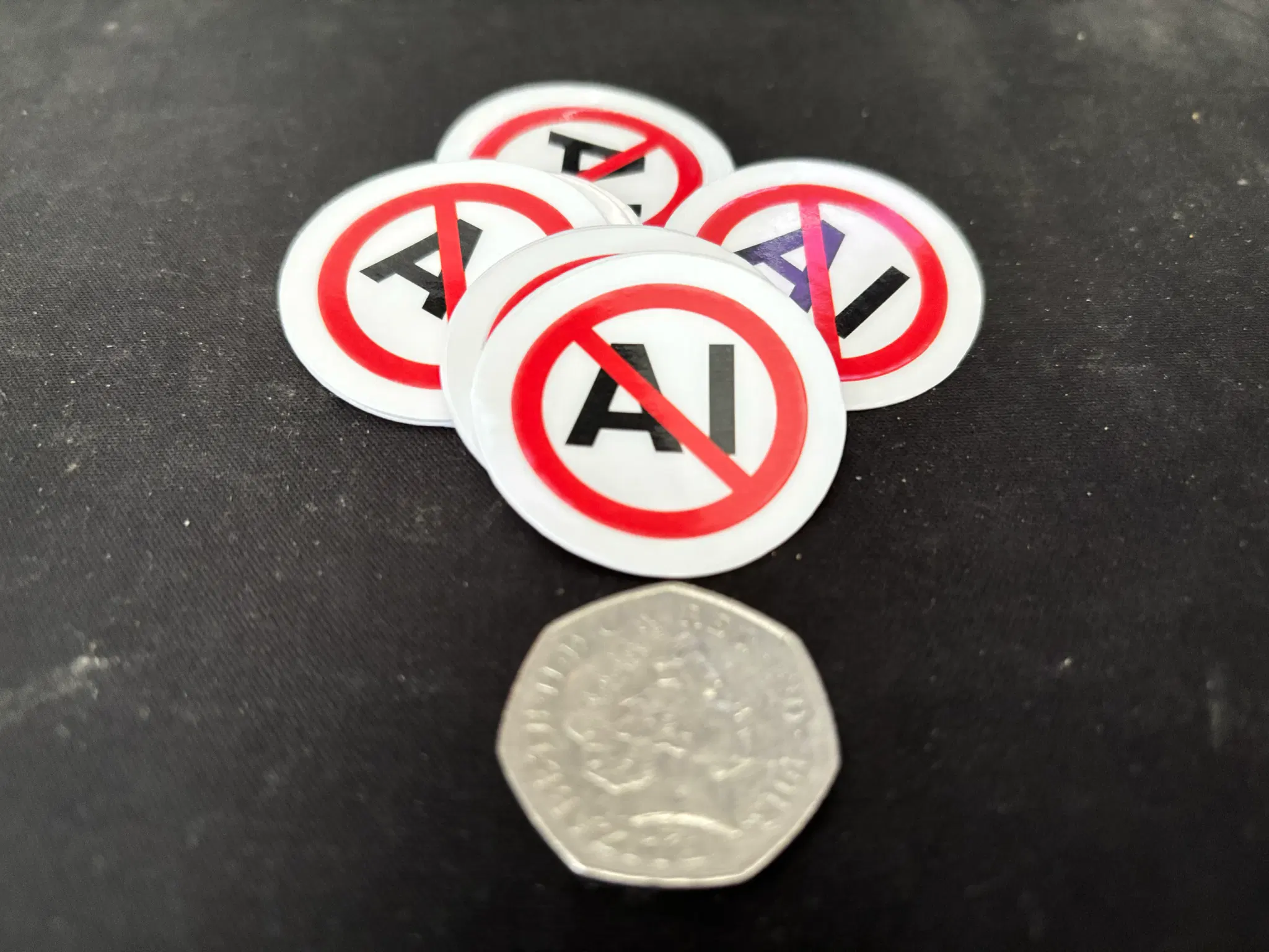 Circle and Red Cross with black text saying AI on a stack of stickers next to a 50 pence price