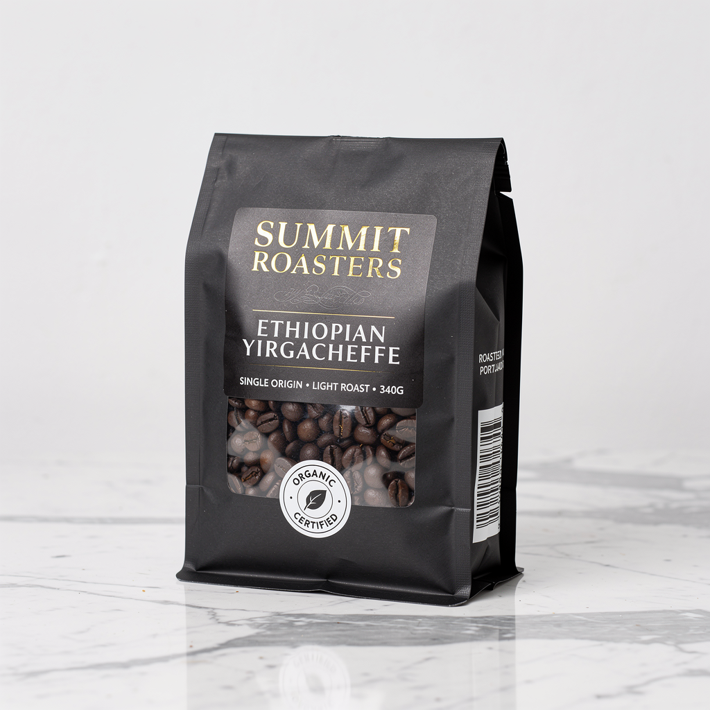 FLUX.2 Pro - Product photography of a premium coffee bag standing upright on a marble countertop, the bag made of matte black kraft paper with a clear window showing whole beans inside, the front label reading SUMMIT ROASTERS in gold foil embossed serif font at the top, below that ETHIOPIAN YIRGACHEFFE in smaller white sans-serif, below that SINGLE ORIGIN * LIGHT ROAST * 340G in even smaller caps, a circular certification stamp reading ORGANIC CERTIFIED in a ring around a leaf icon, on the side of the bag a barcode and the text ROASTED IN PORTLAND OR