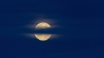 Brilliant full moon rising through wispy clouds dark blue sky