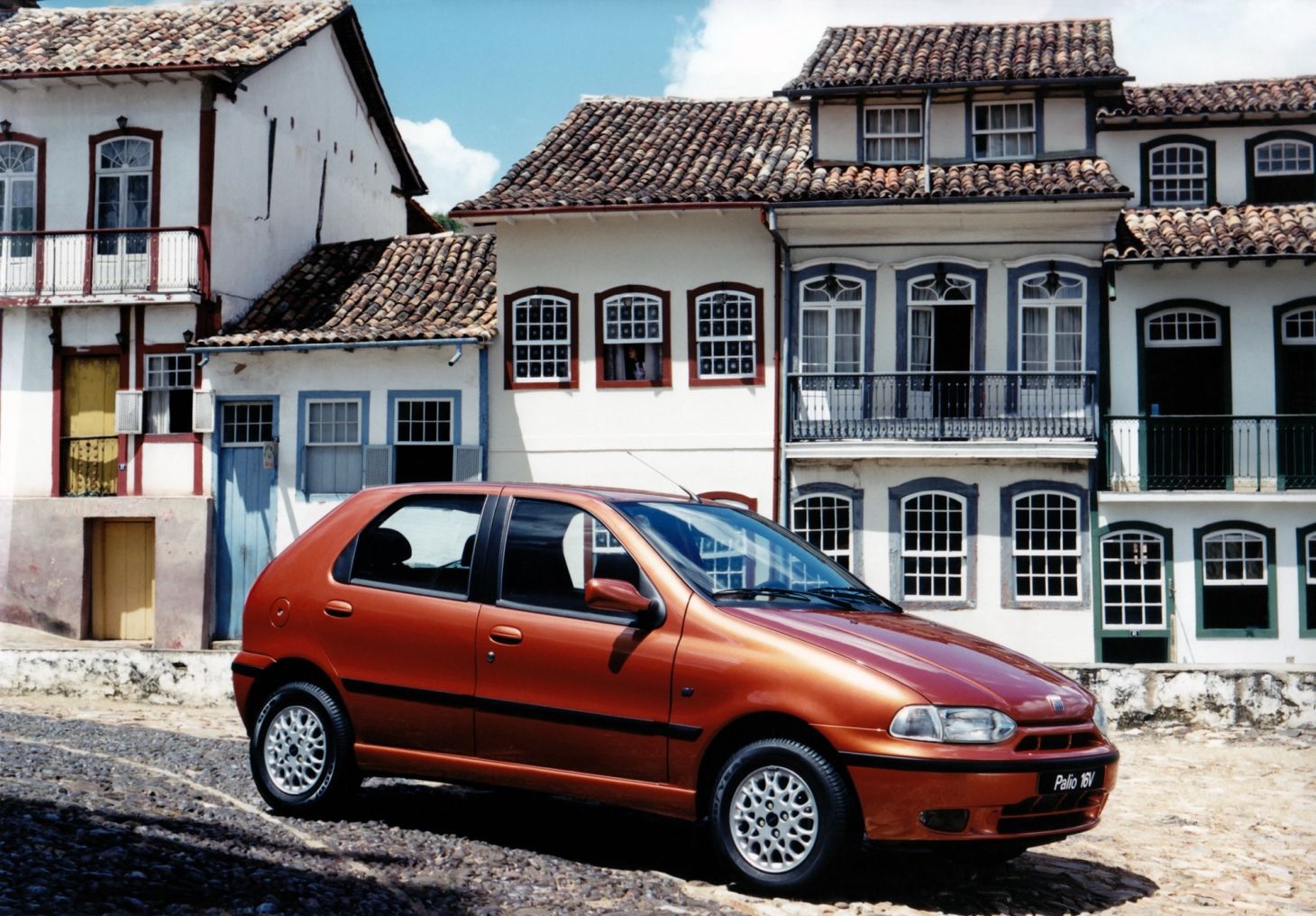 8f38c058-fiat-palio-16v-1996-vermelho-de-frente-com-casario-colonial-ao-fundo