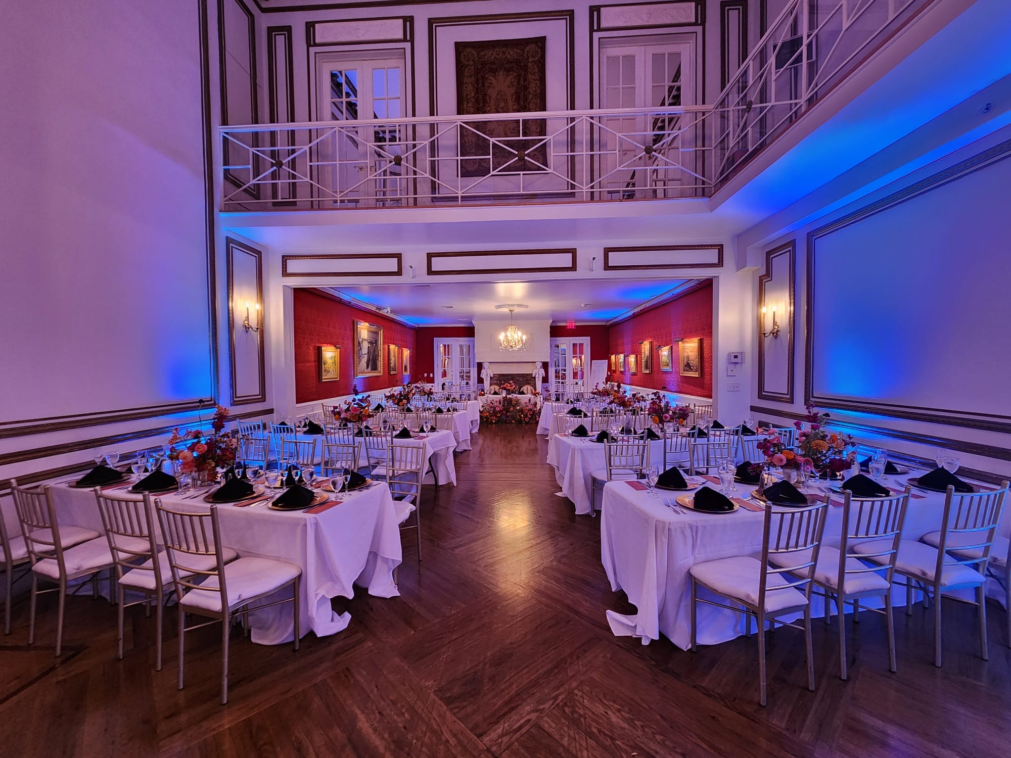 Grand ballroom with high ceilings and upper balcony set with long dinner tables